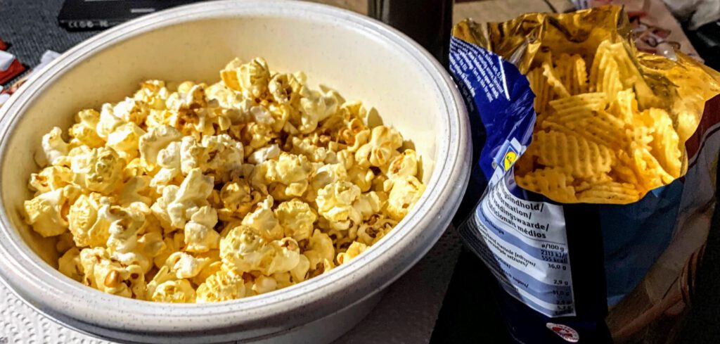 Popcorn in weißer Plastikschüssel neben Chips in der Tüte