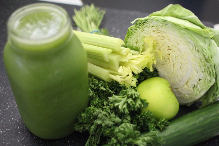 Grünes Obst und Gemüse liegt auf einem Tisch, daneben steht ein grüner Smoothie