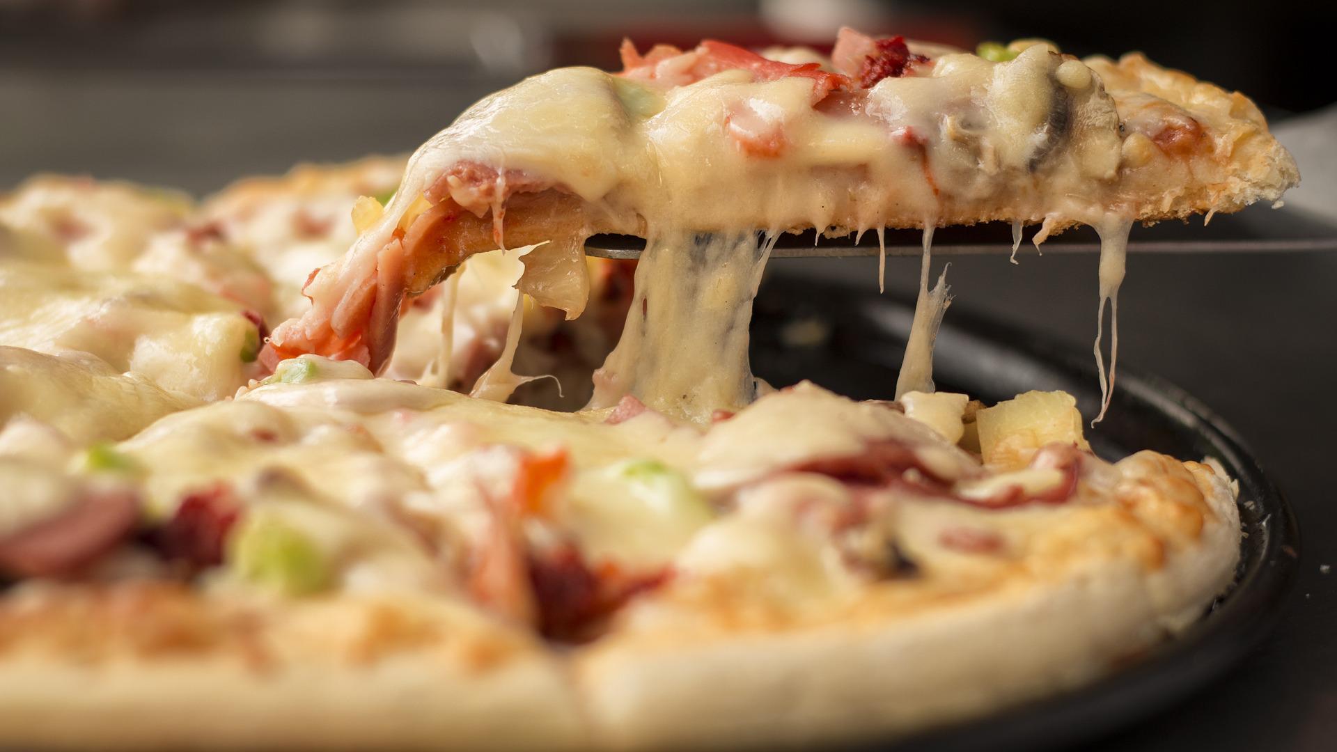 Ein Pizzastück wird herausgehoben, geschmolzener Käse zieht Fäden.